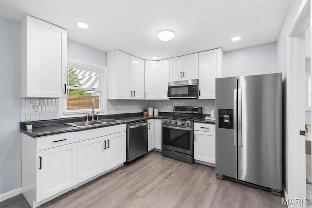 449 Hillcrest Blvd, Ballwin, MO 63021 - kitchen featuring stainless steel appliances, a sink, dark countertops, light wood finished floors, and white cabinetry