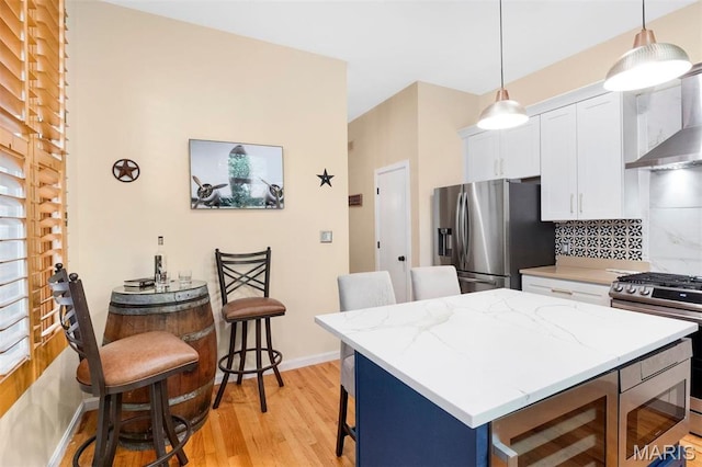 2209 Park Ave, Saint Louis, MO 63104 - kitchen featuring stainless steel refrigerator with ice dispenser, gas stove, wall chimney exhaust hood, a kitchen bar, and white cabinets