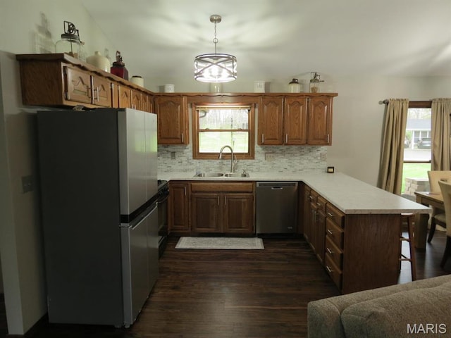 kitchen featuring stainless steel appliances, a sink, a peninsula, dark wood-style flooring, and light countertops