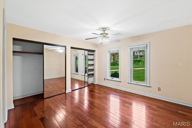 unfurnished bedroom with two closets, hardwood / wood-style flooring, baseboards, and a ceiling fan