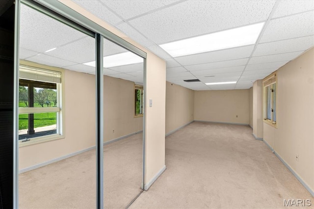 below grade area with a paneled ceiling, carpet flooring, and baseboards
