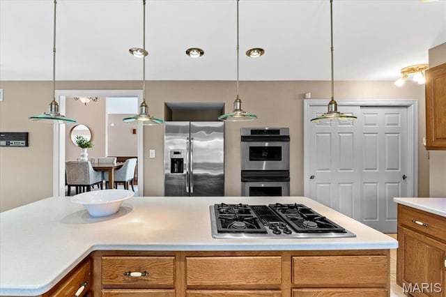 kitchen featuring stainless steel appliances, light countertops, pendant lighting, brown cabinetry, and a kitchen island