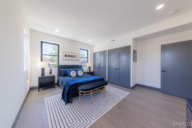 bedroom with baseboards, light wood-style floors, multiple closets, and recessed lighting
