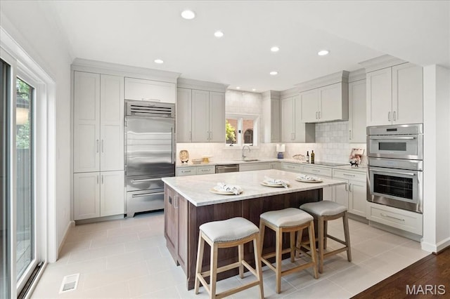139 N Central Ave Unit P, Saint Louis, MO 63105 - kitchen with appliances with stainless steel finishes, a breakfast bar area, tasteful backsplash, a kitchen island, and recessed lighting