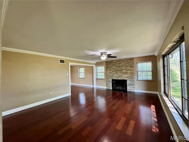 unfurnished living room with dark wood-style floors, ceiling fan, baseboards, a stone fireplace, and crown molding