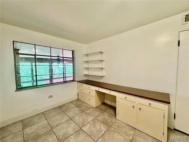 unfurnished office featuring built in desk, light tile patterned floors, and baseboards