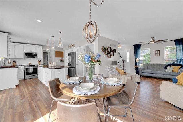 dining room with stairs, light wood-style flooring, a ceiling fan, a chandelier, and recessed lighting