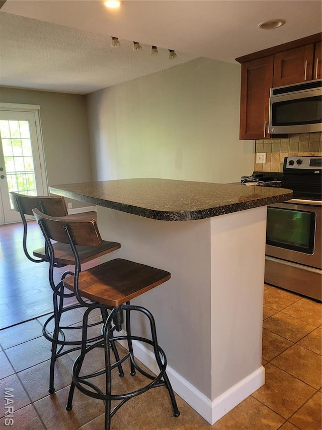 12859 Town And Four Dr Unit 12859, Creve Coeur, MO 63141 - kitchen with appliances with stainless steel finishes, dark countertops, decorative backsplash, a breakfast bar area, and tile patterned flooring