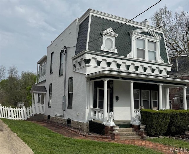 view of front facade with covered porch, fence, mansard roof, and brick siding
