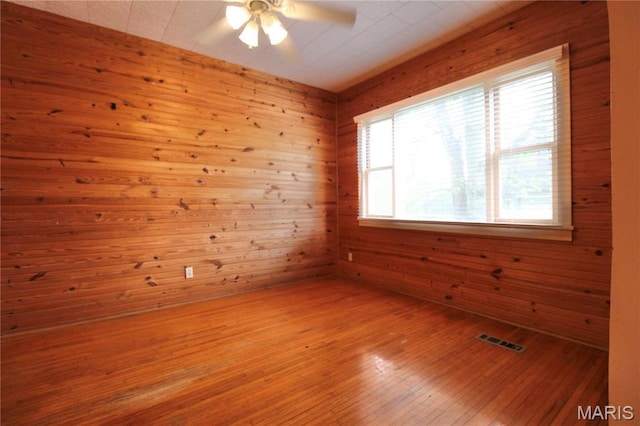 unfurnished room with plenty of natural light, ceiling fan, hardwood / wood-style flooring, and wooden walls