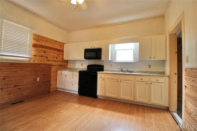 kitchen with black appliances, a sink, light countertops, light wood-type flooring, and wood walls