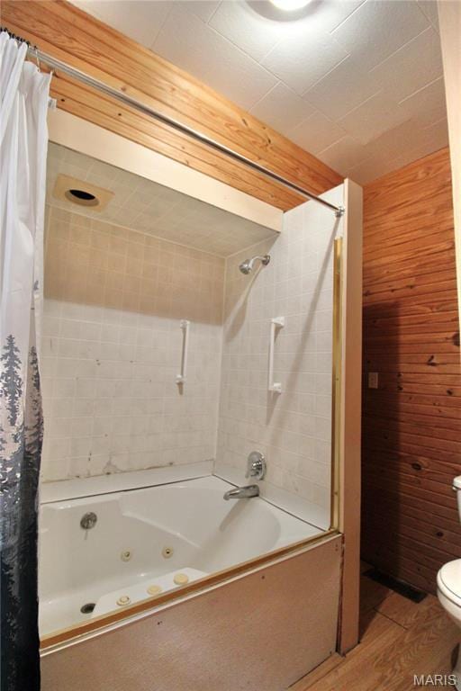 full bath featuring wood finished floors, a combined bath / shower with jetted tub, wooden walls, and toilet