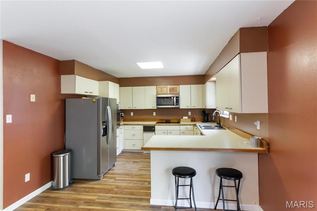 14276 State Route 21, De Soto, MO 63020 - kitchen featuring appliances with stainless steel finishes, a sink, a peninsula, light wood finished floors, and a kitchen bar