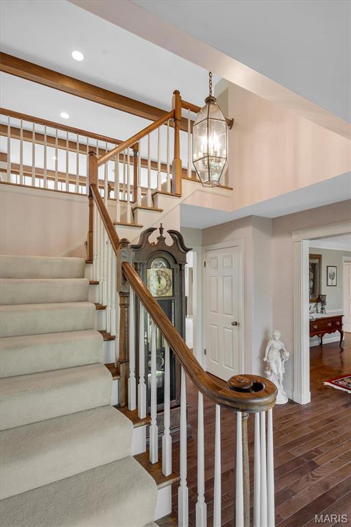 staircase featuring wood finished floors, a towering ceiling, a chandelier, recessed lighting, and baseboards
