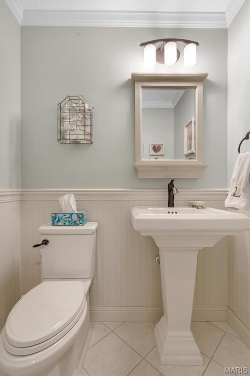 bathroom with tile patterned floors, toilet, wainscoting, baseboards, and ornamental molding