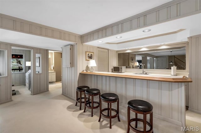 kitchen featuring a sink, a kitchen breakfast bar, baseboards, stainless steel microwave, and crown molding