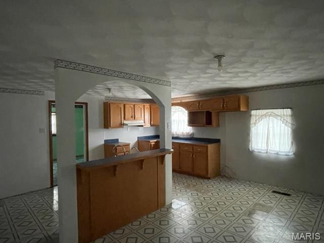 515 S Main St, Fredericktown, MO 63645 - kitchen with brown cabinets, arched walkways, dark countertops, under cabinet range hood, and light floors