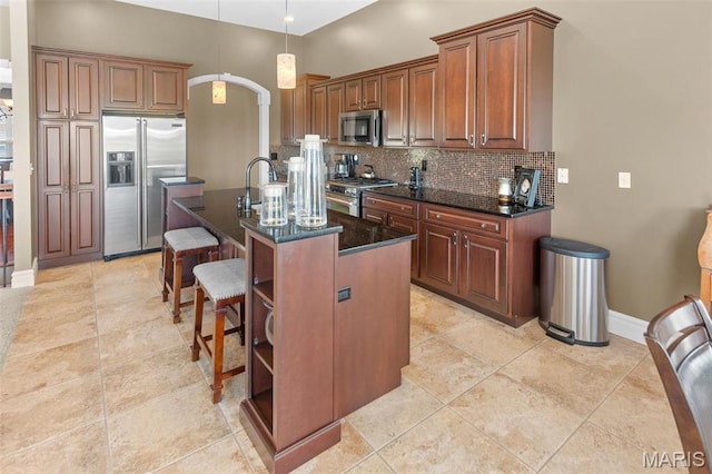 7048 Alston Ct, Edwardsville, IL 62025 - kitchen featuring high end appliances, backsplash, a kitchen breakfast bar, arched walkways, and an island with sink