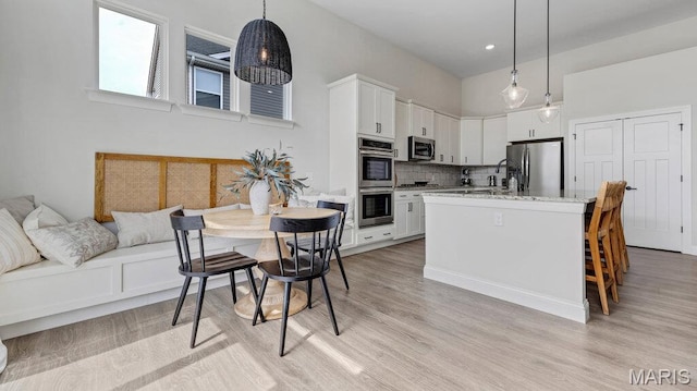 kitchen featuring stainless steel appliances, tasteful backsplash, light wood-style floors, white cabinets, and a towering ceiling