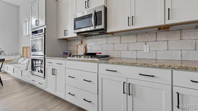 kitchen with stainless steel appliances, backsplash, light stone counters, and white cabinets