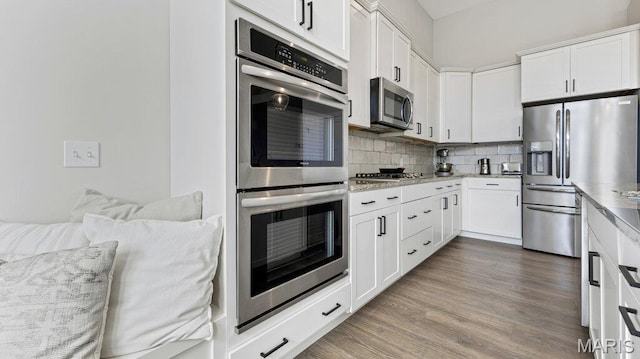 kitchen with appliances with stainless steel finishes, wood finished floors, decorative backsplash, white cabinets, and light stone countertops