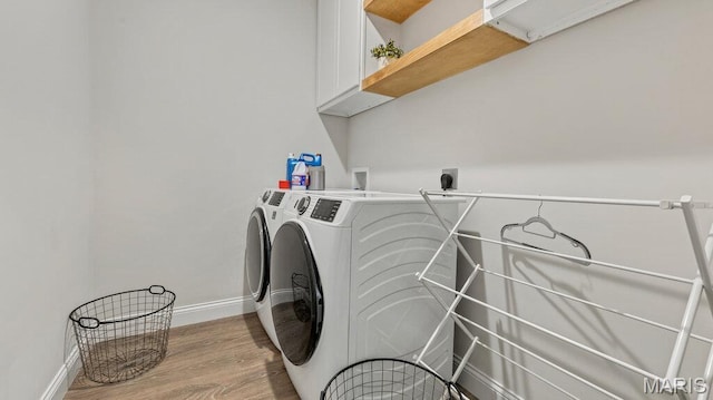 washroom featuring washing machine and dryer, cabinet space, baseboards, and light wood-type flooring