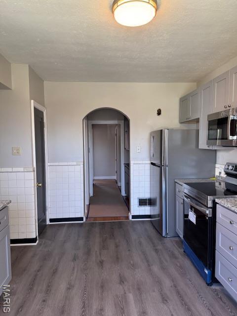 kitchen featuring stainless steel appliances, arched walkways, dark wood finished floors, gray cabinetry, and a textured ceiling