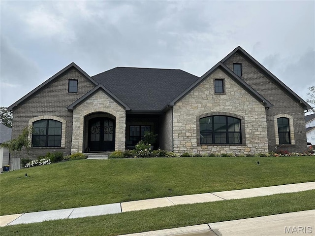 11906 Santino Ct, Creve Coeur, MO 63141 - french country style house featuring stone siding, a front yard, french doors, roof with shingles, and brick siding