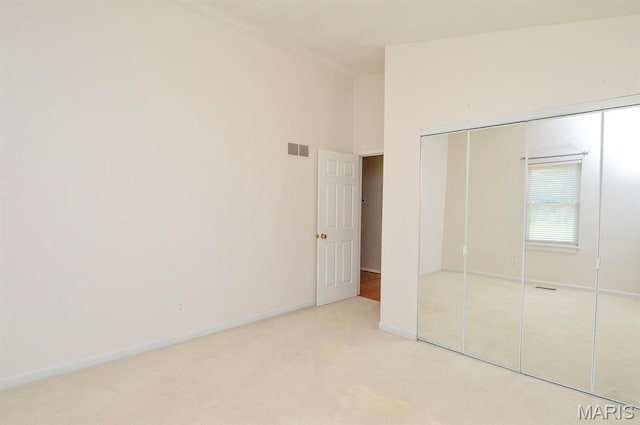 unfurnished bedroom with light carpet, a closet, baseboards, and lofted ceiling