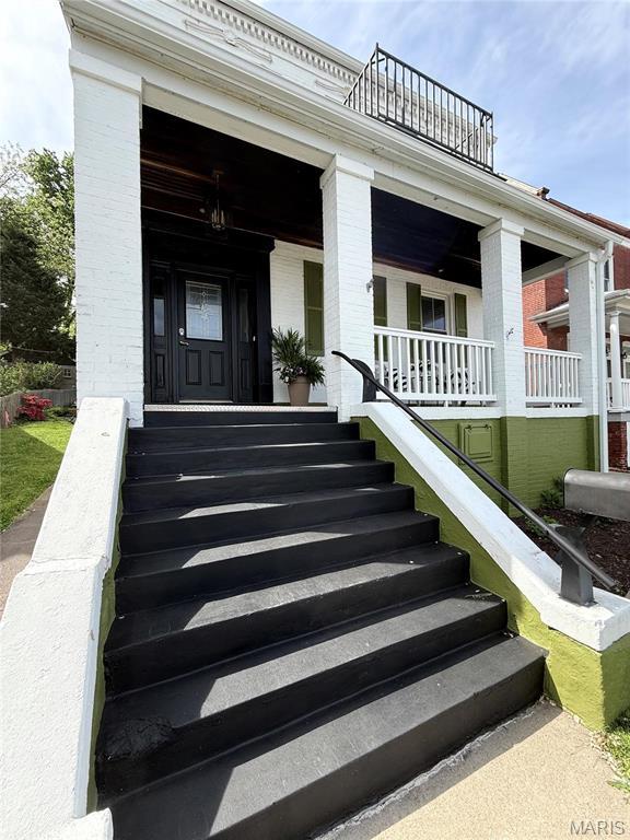 doorway to property featuring a balcony, brick siding, and a porch