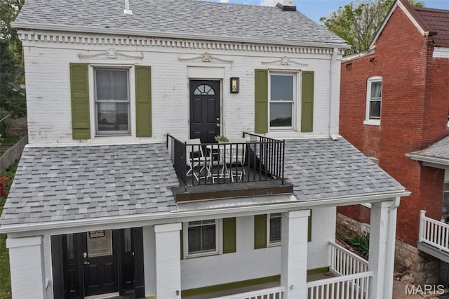 view of front facade featuring a balcony, brick siding, and a shingled roof