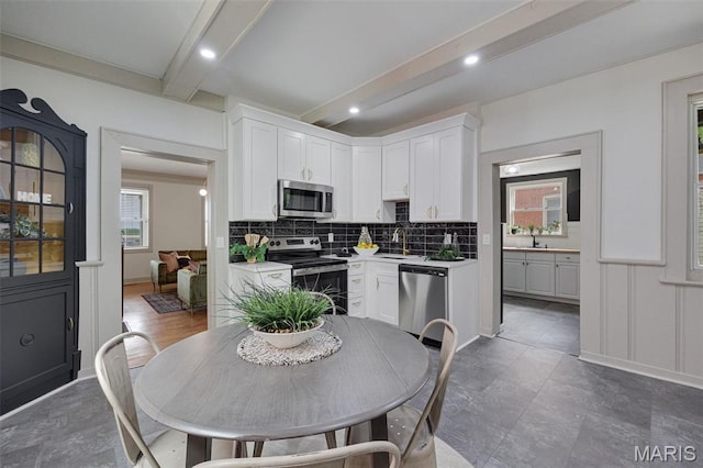 kitchen featuring stainless steel appliances, a sink, beamed ceiling, decorative backsplash, and white cabinets