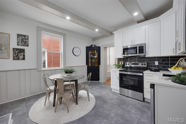 kitchen with stainless steel appliances, a sink, beamed ceiling, light countertops, and white cabinets
