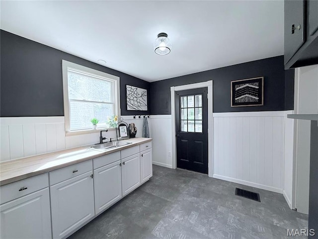 kitchen featuring a sink, wainscoting, healthy amount of natural light, light countertops, and white cabinetry