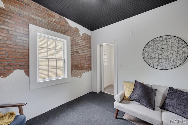 carpeted living room featuring brick wall