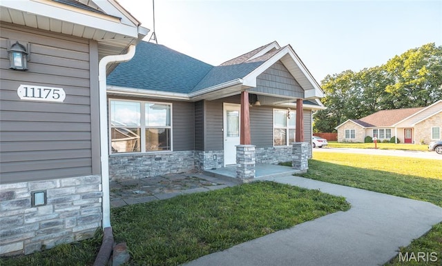 11175 Lexington Ln, Rolla, MO 65401 - view of exterior entry featuring stone siding, a lawn, covered porch, and roof with shingles