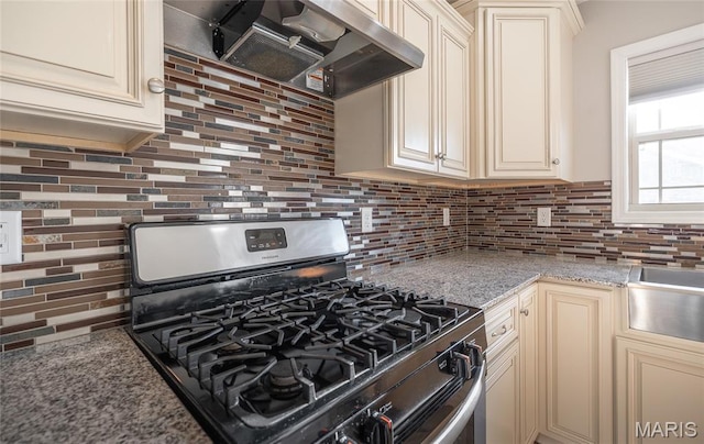 11175 Lexington Ln, Rolla, MO 65401 - kitchen with stainless steel gas range, cream cabinetry, under cabinet range hood, backsplash, and light stone counters