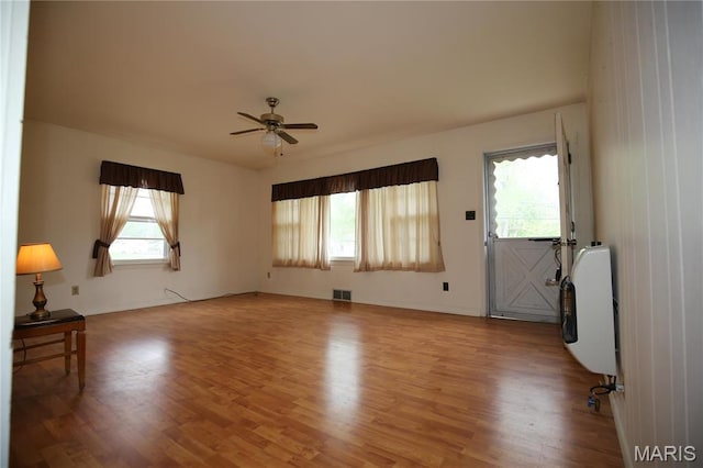 spare room with heating unit, light wood finished floors, a ceiling fan, and baseboards