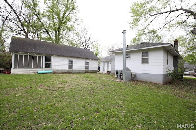 rear view of house with a sunroom, a chimney, and a lawn