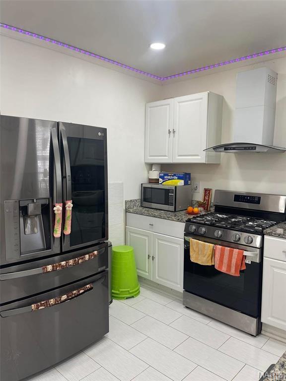 4007 Delor St, Saint Louis, MO 63116 - kitchen with appliances with stainless steel finishes, wall chimney range hood, white cabinetry, light tile patterned flooring, and dark stone counters