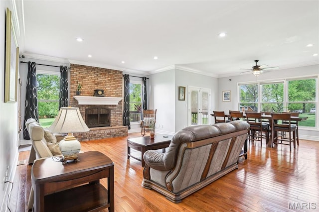 living area with ornamental molding, ceiling fan, hardwood / wood-style flooring, a brick fireplace, and recessed lighting