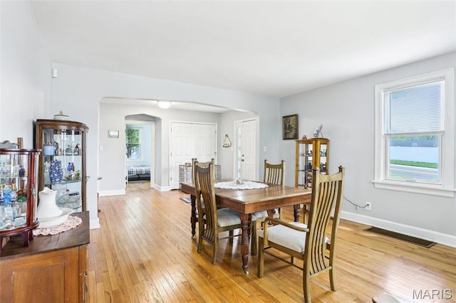dining room with arched walkways, light wood-type flooring, and baseboards