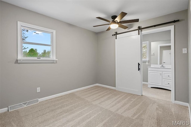 1399 Valli Ln, Saint Charles, MO 63304 - unfurnished bedroom featuring a barn door, carpet flooring, baseboards, a sink, and ensuite bathroom