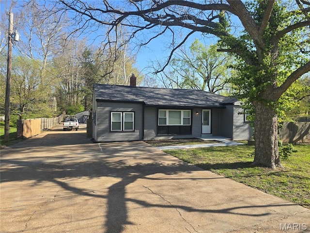 view of front of home with concrete driveway, fence, and a chimney