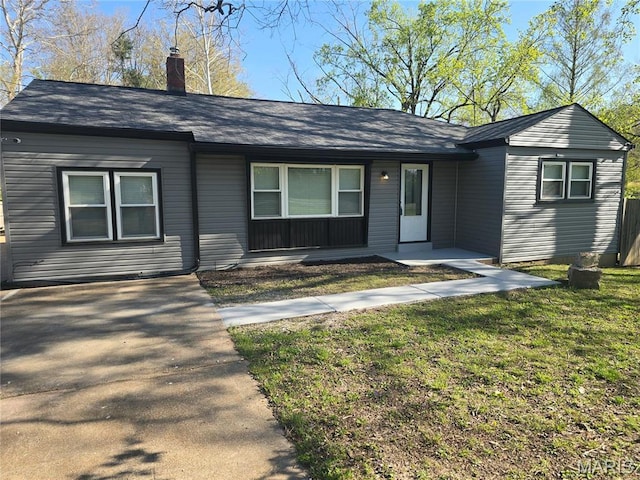ranch-style house with a front yard, a chimney, roof with shingles, and a porch