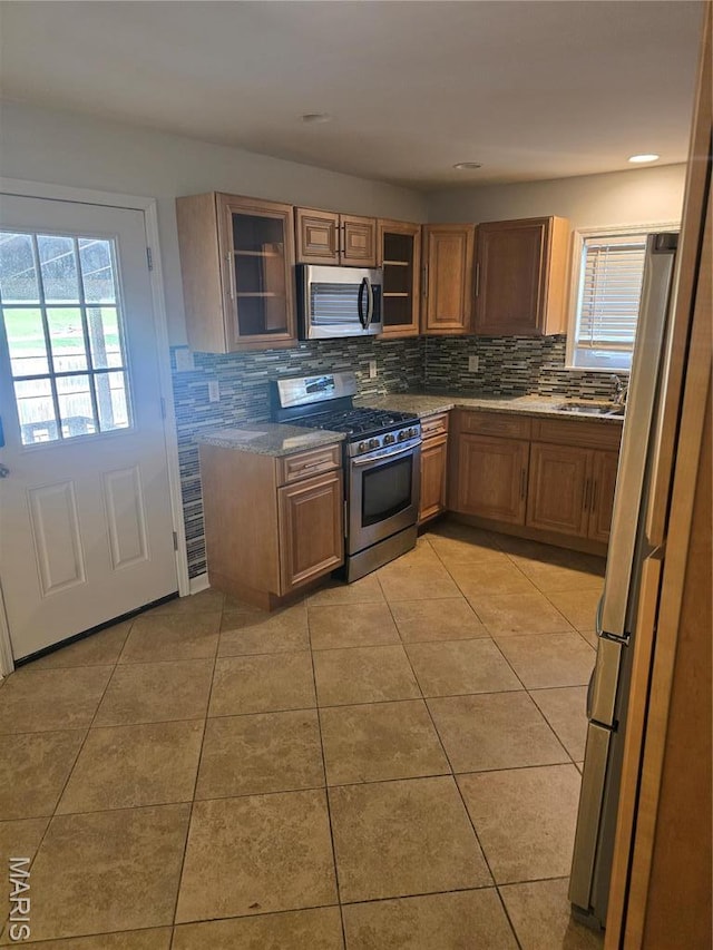 kitchen featuring appliances with stainless steel finishes, tasteful backsplash, light tile patterned floors, and brown cabinetry