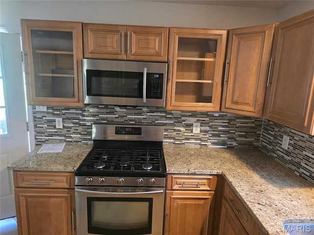 kitchen with appliances with stainless steel finishes, decorative backsplash, glass insert cabinets, and light stone counters