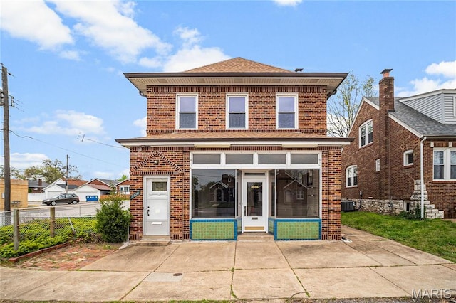 view of front facade with a sunroom, brick siding, central air condition unit, and fence