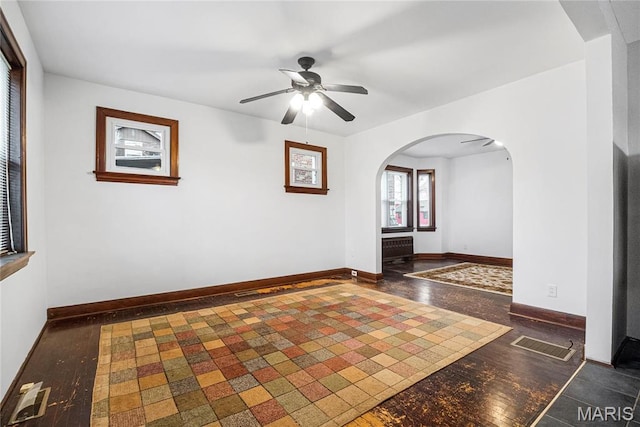 unfurnished room with arched walkways, ceiling fan, baseboards, radiator heating unit, and wood finished floors