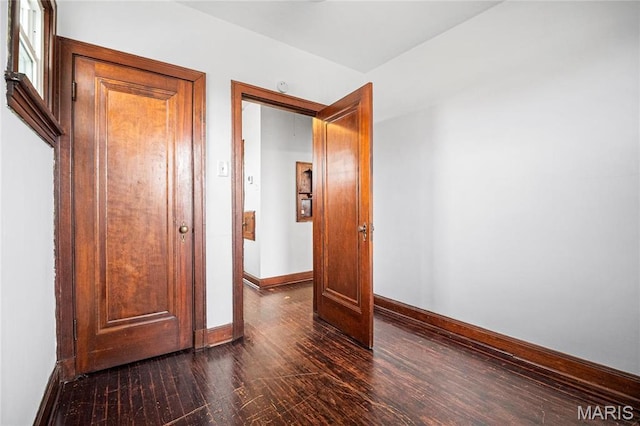 empty room featuring baseboards and dark wood finished floors